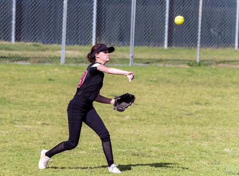 Skilled Teenage Softball Player Releasing A Quick Throw After Making A Defensive Catch In The Outfield.