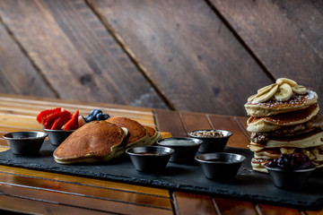 platter of pancakes with . double large stack of protein pancakes and array of different toppings on the side including strawberries blueberries maple syrup granola and sour cream 
