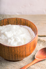 Close-up wooden bowl with yogurt and wooden spoon on burlap on wooden table. 