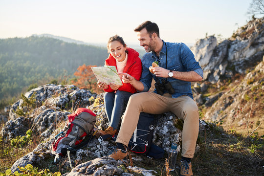 Happy couple on a hiking trip in the mountains taking a break looking at map