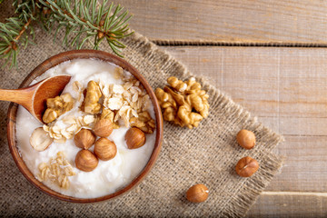 Wooden bowl with yogurt with rolled oats and nuts, on burlap napkin on rustic wooden table.