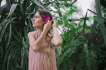 Portrait of young beautiful woman with purple tropical flower in long hair in tropical forest