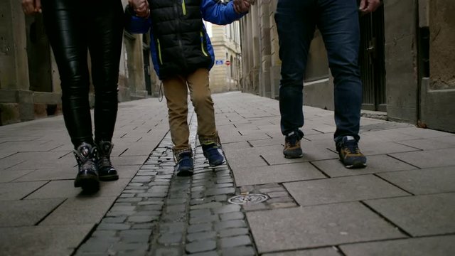 Big Friendly Family - Mom, Dad And Son Walking On The Street On The Sidewalk Among The Houses And Holding Hands.