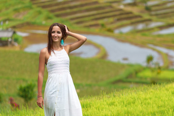 Fototapeta na wymiar Tanned girl in a white dress posing on the background of rice fields. Close up