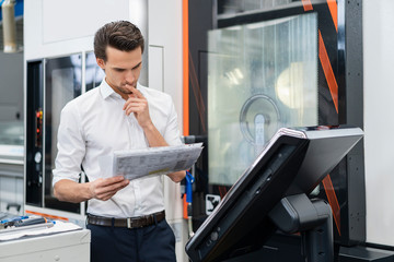 Businessman reading manual at a machine in a factory