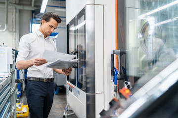 Businessman reading manual at a machine in a factory