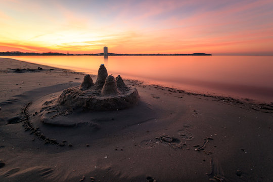 Sandburg, die von einem Kind gebaut wurde, bei einem farbenfrohen Sonnenuntergang