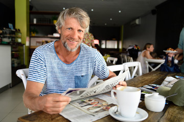 Portrait of smiling mature man sitting in a coffee shop reading newspaper