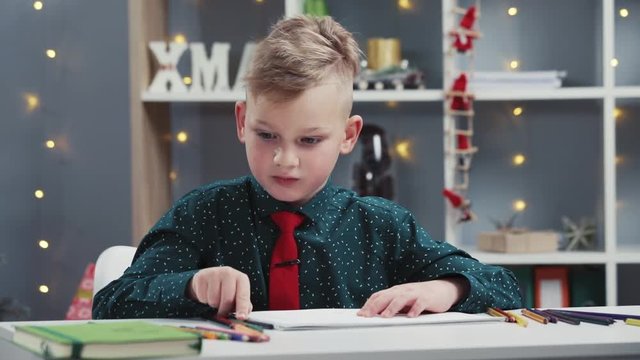 Close up view of stylish little boy with a red tie and black shirt focused on painting, choosing the right colored pencil. Art class, art therapy, talent, working hard. Childhood education concept