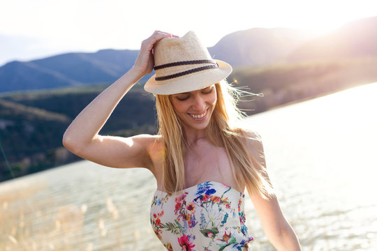 Smiling young woman wearing summer hat and top with floral design in front of lake