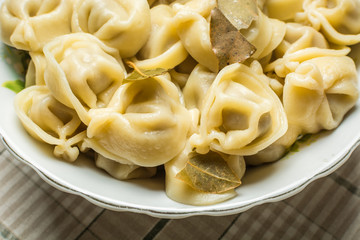 Handmade boiled shaped dumplings with bay leaves in large plate on kitchen table.