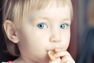 Beautiful child with big blue eyes eating orange slice