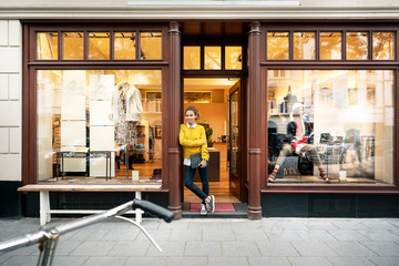 Young woman standing in door of a fashion store, holding laptop