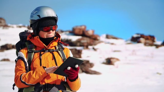 climber in a special outfit stands on a snow-covered slope and checks the route on a map on your tablet