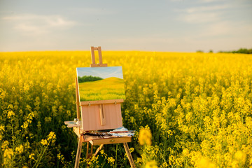easel with paints and canvas painting in the field