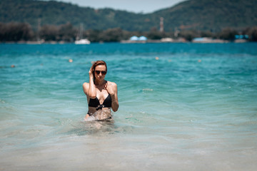 A young beautiful girl in black sunglasses and black bikini staying in blue water in the sea ,enjoying beach holiday