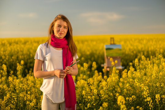 girl painter with an easel in a yellow rapeseed field