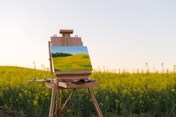easel with paints and canvas painting in the field