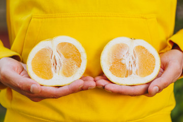 a man in a yellow hoodie is holding two halves of a yellow citrus cut in half. healthy eating, proper nutrition, organic food, close-up, conceptual photo.