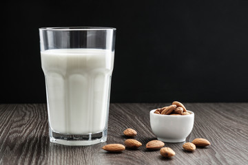 glass of almond milk and almonds nuts in small white bowl scattered on the table
