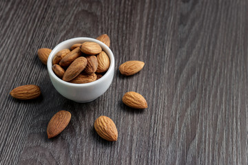 almond nuts in white bowl and scattered on  black wooden background copy space