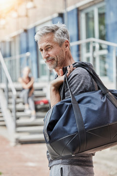 Portrait of mature man with sports bag standing in front of gym