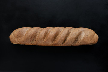 fresh rye baguette bread on black background top view