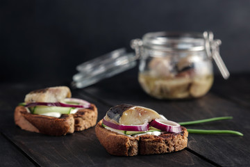 open sandwich with herring cucumber slice red onion rye bread on black wooden table soft focus