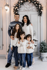 Fototapeta na wymiar Charming family of nice couple with three charming children in blue jeans poses in cozy room with Christmas decor