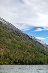 landscape with mountains, green trees and blue lake on a cloudy sky background Altai