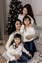 Attractive mother hugs her three beautiful daughters standing in the room with Christmas decor