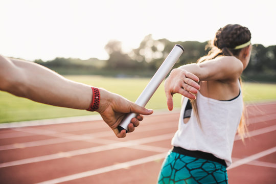 Close Up Of Athlete Hand Passing Baton To Woman Running On Track