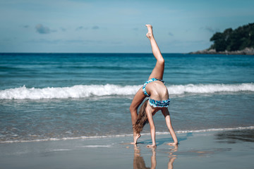 young girl  in blue swimsuit doing gymnastics on beach. Sports on the beach. Relax. The girl makes...