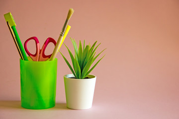 Stationery. Writing accessories pen, pencil, scissors, ruler in a glass on a pink background. Back...