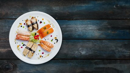 Rotating sashimi set on a white round plate, decorated with small flowers, Japanese food, top view. Wooden background with the copy space for your text