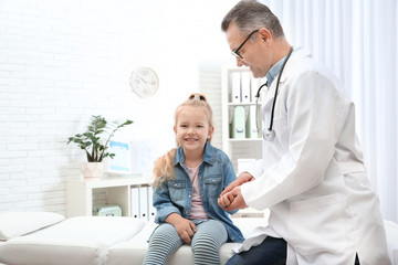 Obraz premium Doctor checking little girl's pulse with fingers in hospital. Space for text
