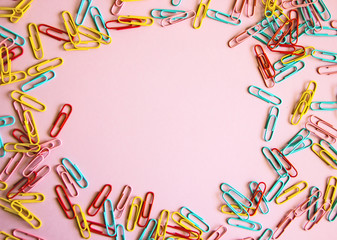 Pink background with colored stationery for paper scattered on it. paper clips on a pink background, office theme. Colorful Back to School background. Top view, flat lay.