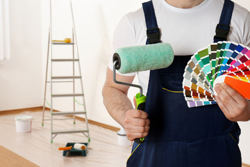 Male decorator with paint roller and color palette samples in empty room, closeup. Space for text - obrazy, fototapety, plakaty