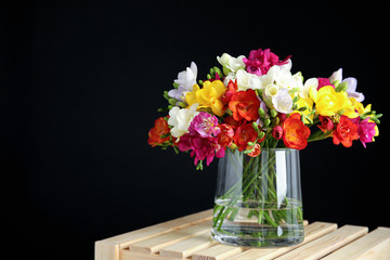 Bouquet of spring freesia flowers in vase on dark background. Space for text