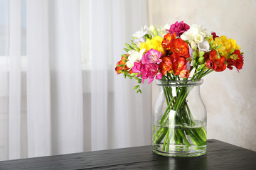 Vase with bouquet of spring freesia flowers on table in room. Space for text