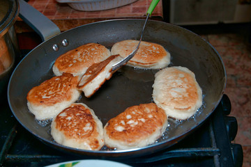 Home cooking food. Fresh tasty fritter or pancakes are fried in a pan and turned over with a fork.