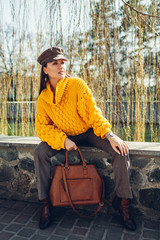 Young woman holding stylish handbag and wearing yellow sweater. Spring female clothes and accessories. Fashion