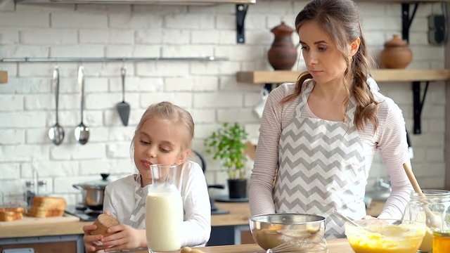 Cute little kid girl pouring milk in to the bowl. Mother and daughter preparing dogh together.