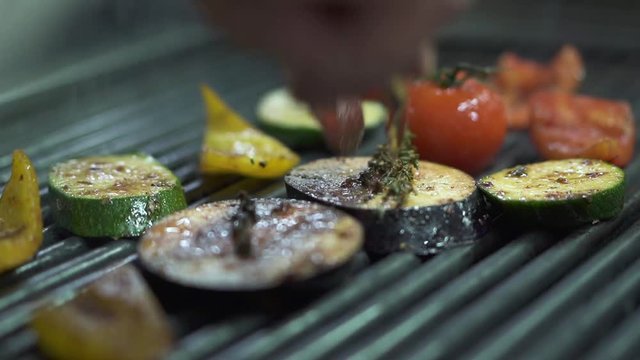Chef hand checking vegetables tomato, eggplant, zucchini, yellow bell pepper on the grill using metal tongs close up. Cook preparing vegetarian food. Healthy lifestyle