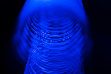 Blue metal spiral / coil spring with blurred background on black. Macro abstract background