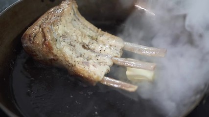 Chef hand adds piece of butter using the spoon in the frying pan with juicy ribs and then takes away the pan. Cook preparing appetizing meat food in modern restaurant. Healthy lifestyle
