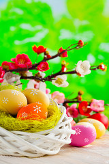 Obraz na płótnie Canvas Easter eggs in the nest on wooden table and flowers on green background