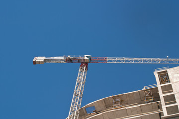 Image of a tower crane and a building under construction against the blue sky