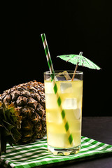 Pineapple cocktail with ice tube and umbrella on a black background. Tropical fruit, summer mood in a dark style.
