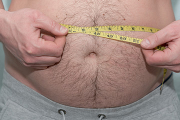 overweight man measures his fat belly with a measuring tape